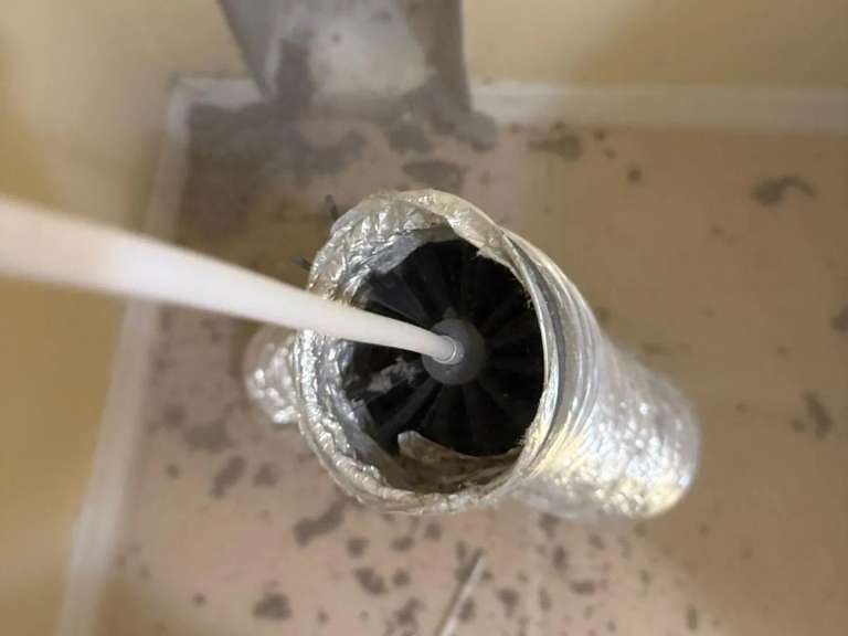 The rotary brush head inside the end of a flexible foil dryer duct during a cleaning