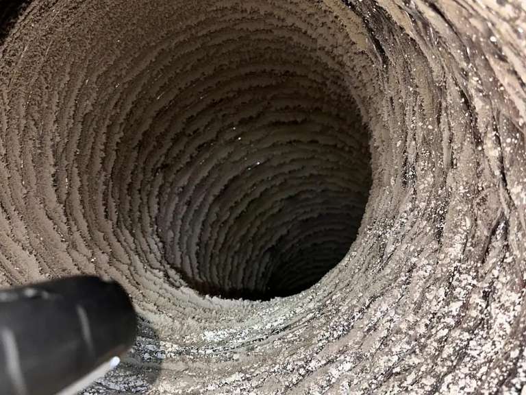 Looking down a dryer duct lined with lint before cleaning, with the brush entering at the edge