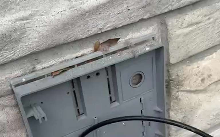 A dryer vent wall box on a stone exterior with its hood taken off for the check, the cleaning cable in front of it