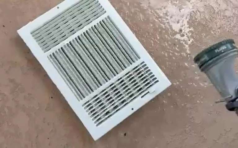 A supply register grille taken down and set on the floor during an air duct cleaning, next to the cleaning equipment