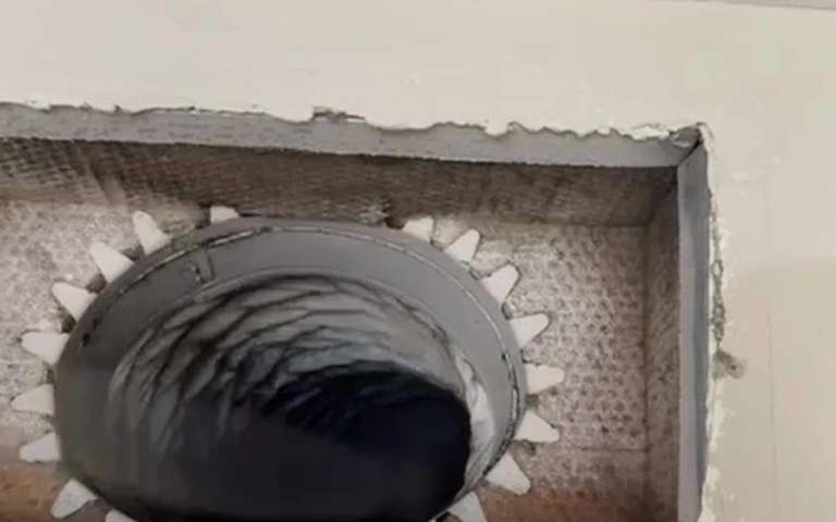 An air duct opened at a ceiling register, with the rotary brush spinning inside the run